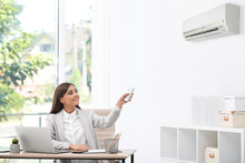 Young Woman With Air Conditioner Remote In Office
