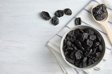 Bowl and spoon of sweet dried plums on table, top view with space for text. Healthy fruit