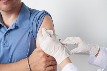 Hands of doctor with syringe giving injection of vaccine to male patient