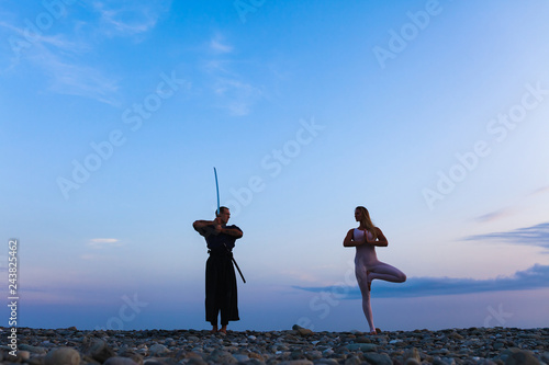 Fotografie, Obraz silhouette of Aikido fighter in traditional costume with sword and woman yoga in