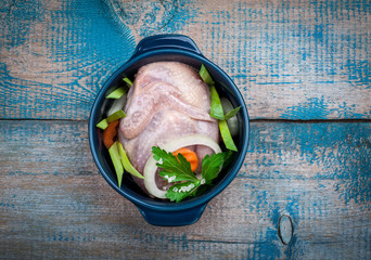 Raw chicken in a pot with vegetables on old wooden table