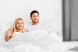 © Syda Productions - people, leisure and rest concept - happy couple lying in bed at home and watching tv