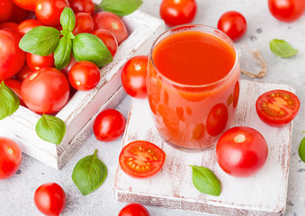 Glass of fresh organic tomato juice with fresh raw tomatoes basil and pepper in box on stone kitchen background