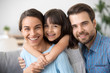 © fizkes - Cheerful beautiful family of three embracing laughing looking at camera, happy cute kid girl hugging smiling mom posing with dad for portrait, child daughter mother and father bonding headshot