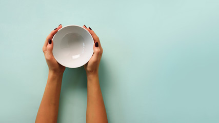 Female hand holding white empty bowl on blue background with copy space. Healthy eating, dieting concept. Banner