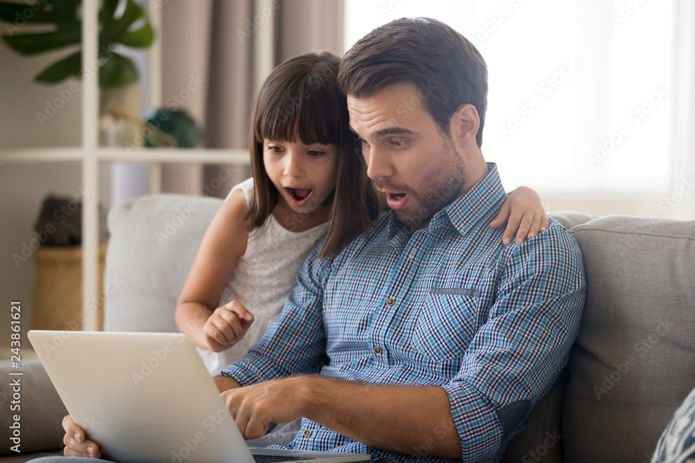 Surprised father and kid girl looking at computer screen using laptop, amazed dad and child daughter excited with unbelievable internet news, shocked by sale offers doing online shopping at home - obrazy, fototapety, plakaty 