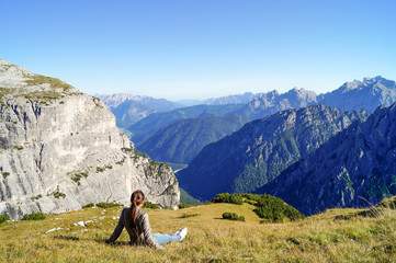 girl sits on the grass and admires the beautiful mountain view in the Alps