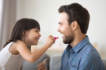 Canvas Print - Happy father and kid girl laughing doing makeup together, little daughter puts lipstick on dads lips, funny child applying make-up on daddys face having fun playing enjoying time with parent at home