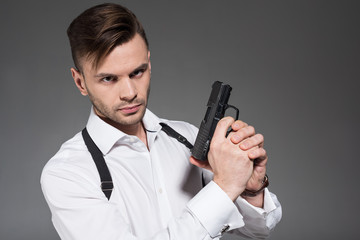 handsome secret agent with holster holding handgun, isolated on grey