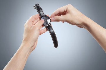 Hands setting the wrist watch on gray background