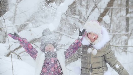 Wall Mural - Winter forest. Two happy little girls standing next to each other and throws snow up