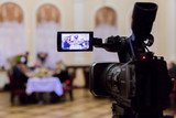 Fototapeta  - Video shooting at the event in the restaurant. Digital video camera with LCD display. People sit at tables in the background. Defocused background.