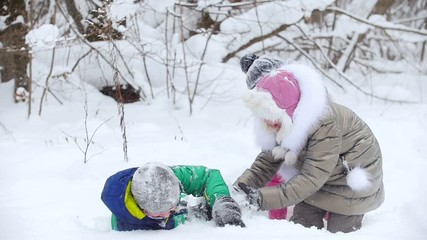 Wall Mural - Winter forest. Smiling children in bright clothes playing with snow. Two little girls buried in the snow their brother