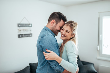 Wall Mural - Relationship goals. Beautiful young wife and husband hugging and smiling while standing at home.