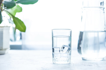 Wall Mural - glass cup and carafe with water and ice on a white table