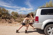 © ML Harris - Gritty, strong young women with car trouble pushing disabled vehicle SUV on road