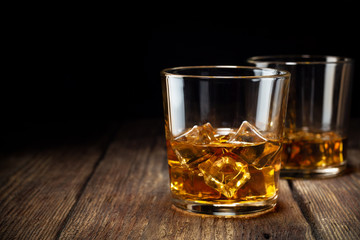 Two glass of whiskey with ice on wooden table. Copy space for text.