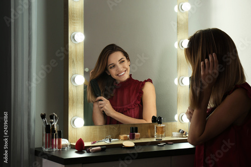 Fotomural Woman brushing hair near mirror with light bulbs in dressing room