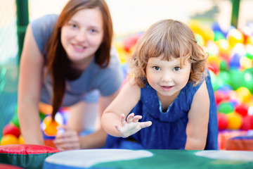 Happy little girl having fun in colourful plastic balls pool with her mother