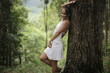 © emaria - Beautiful woman in white dress lean on tree trunk in forest posing to camera