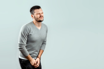 A young, attractive man feels pain in his groin, arms folded between his legs. Experiencing pain, male problems, potency.