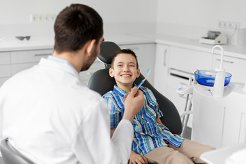 Sticker - medicine, dentistry and healthcare concept - male dentist giving toothbrush to kid patient at dental clinic