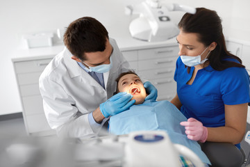 Poster - medicine, dentistry and healthcare concept - dentist with mouth mirror checking for kid patient teeth at dental clinic