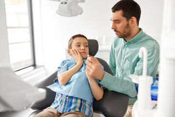 Sticker - medicine, dentistry and healthcare concept - father supporting son suffering from toothache at dental clinic