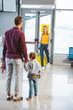 © LIGHTFIELD STUDIOS - back view of man holding hands with daughter and looking at wife with luggage