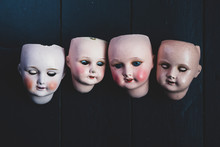 Close Up Of Four Porcelain Dolls' Heads On Black Background.