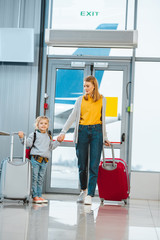 Wall Mural - cheerful mother looking at daughter while holding hands in airport