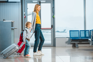 Wall Mural - mother and daughter holding hands and walking with baggage in airport