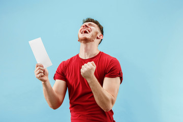 Young boy with a surprised happy expression bet slip on blue studio background. Human facial emotions and betting concept. Trendy colors