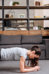 Wall Mural - focused sportswoman doing plank exercise at home in living room