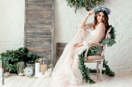 Cuadros en Lienzo A girl in a beige peignoir, with a wreath of flowers on her head, poses in the s
