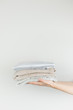 © Photoboyko - Heap of clothes in female hands. Neatly stacked clothing at white background and vertical copyspace.