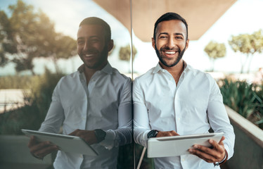 Indian businessman standing outside building with a tablet looking into camera