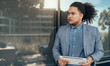 © JonoErasmus - Young mixed race guy with curly afro holding a tablet looking into the distance with reflection on glass wall