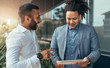© JonoErasmus - Two trendy businessmen talking and laughing casually outside, pointing and using a digital tablet