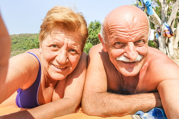 Wall Mural - Senior happy couple taking selfie at beach resort in Thailand trip on tropical tour - Adventure and fun concept of active elderly around the world - Hot sunny day with warm saturated filtered tones