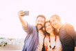 © simona - Bright yellow filter group of caucasian 40 years old people men and woman taking selfie picture with smart phone device - backlight and white sky in bnackground - happy leisure activity toncept