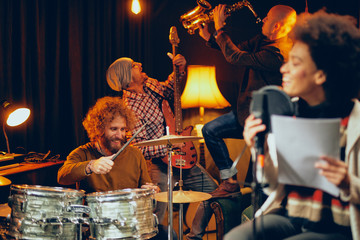 Wall Mural - Mixed race woman singing. In background band playing instruments. Home studio interior.