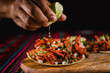 Close-up of a lime being squeezed in a mexican taco, with traditional colorful background