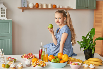 The girl eats fruit pineapple, watermelon, apples and drinks drinks from chia. Healthy food in the children's menu. Happy child with fruits and fresh juice in kitchen, kids healthy eating concept