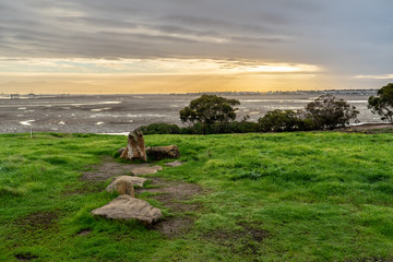 Rocks and grass on a hilly terrain with the sizing sun peeking through the clouds, Bedwell Bayfront Park, Menlo Park, California