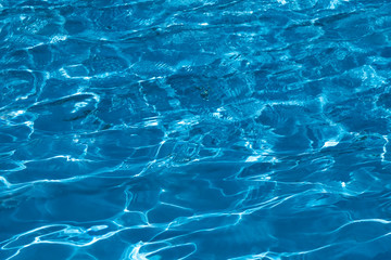 blue and bright ripple water surface in swimming pool with sun reflection.