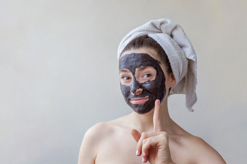 Wall Mural - Beauty portrait of woman in towel on head applying black nourishing mask on face on white background isolated. Skincare cleansing spa relax cosmetics concept