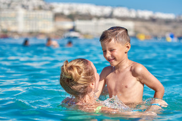 Mom and son are playing in the sea, they are happy to spend their summer holidays on the seacoast.