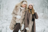 Fototapeta Las - Portrait of two happy blonde women in hat on walk in winter forest