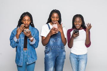 Wall Mural - Portrait of pretty charming african women surprised using phones isolated on white background